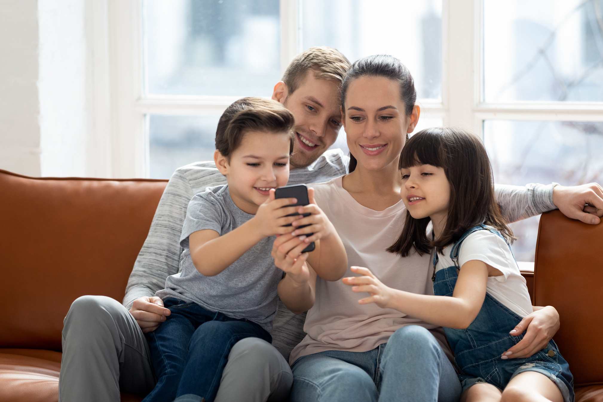 Excited family hugging, entertaining, using mobile phone.